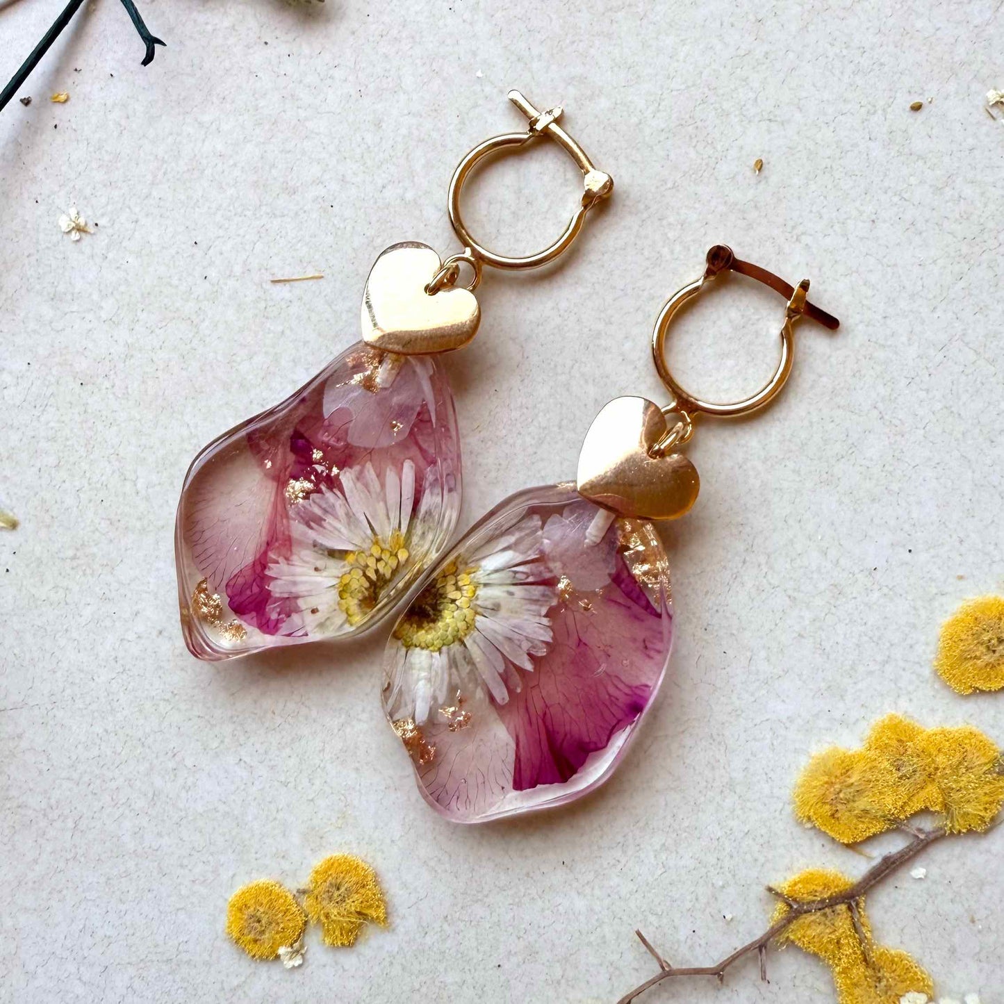 Par de aros Petrohue con fondo blanco. Cápsulas con flor margarita y pétalos de adelfa.