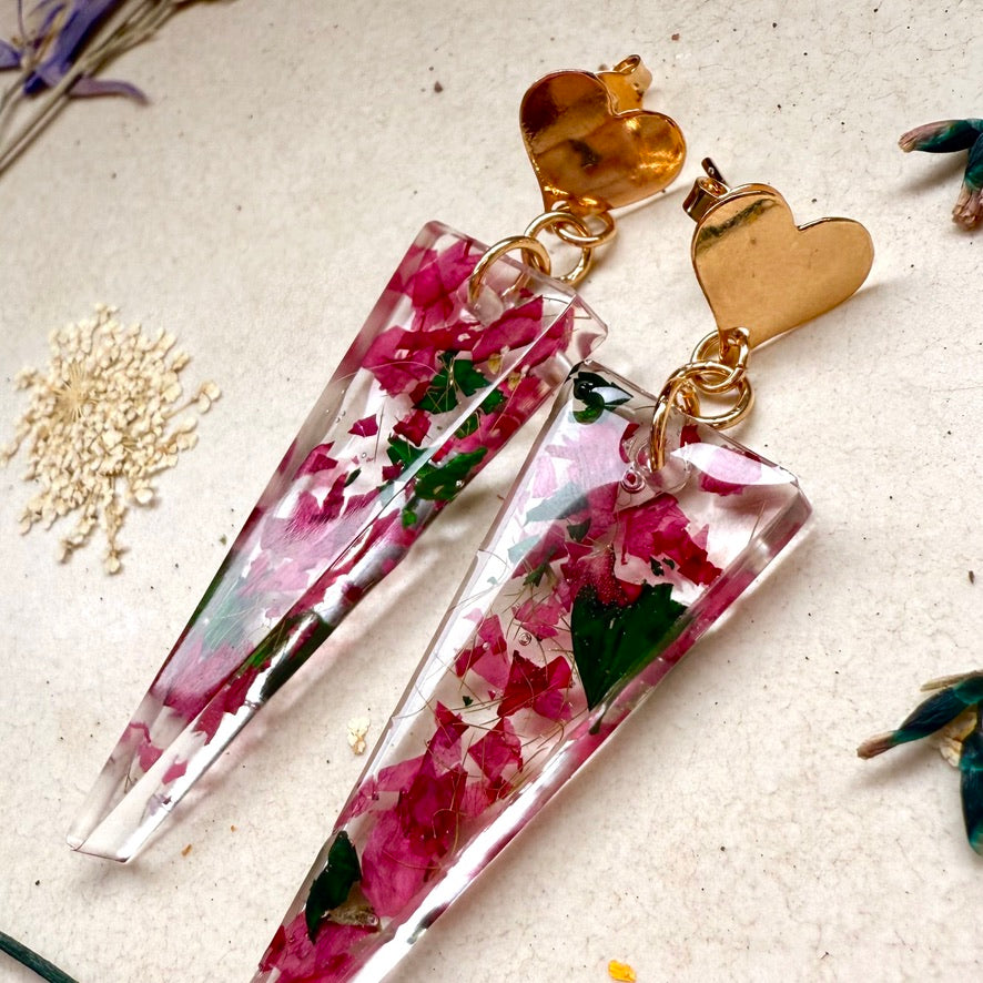 vista lateral Par de aros Caldera, cápsula triangular con pétalos color rosado de hortensia. Broche con forma de corazón.