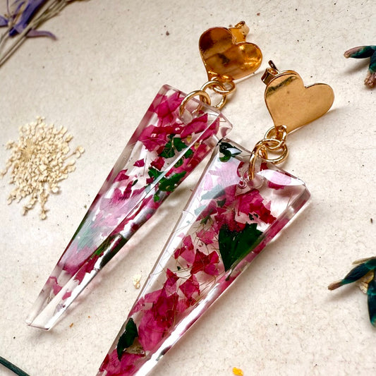 vista lateral Par de aros Caldera, cápsula triangular con pétalos color rosado de hortensia. Broche con forma de corazón.