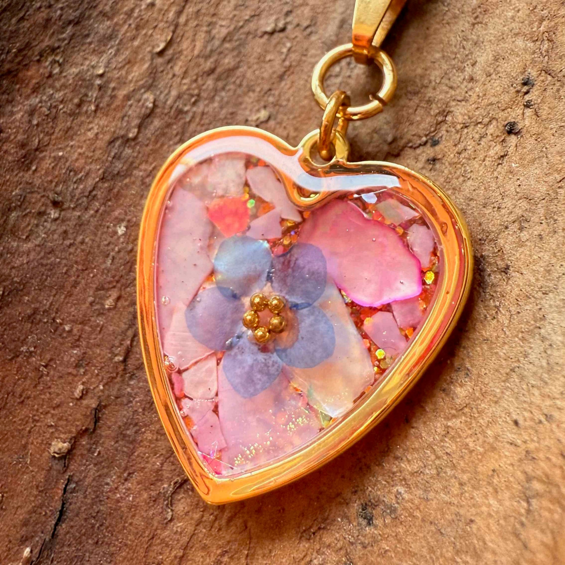 zoom de collar Candelaria con forma de corazón, fondo rozado y flor no me olvides