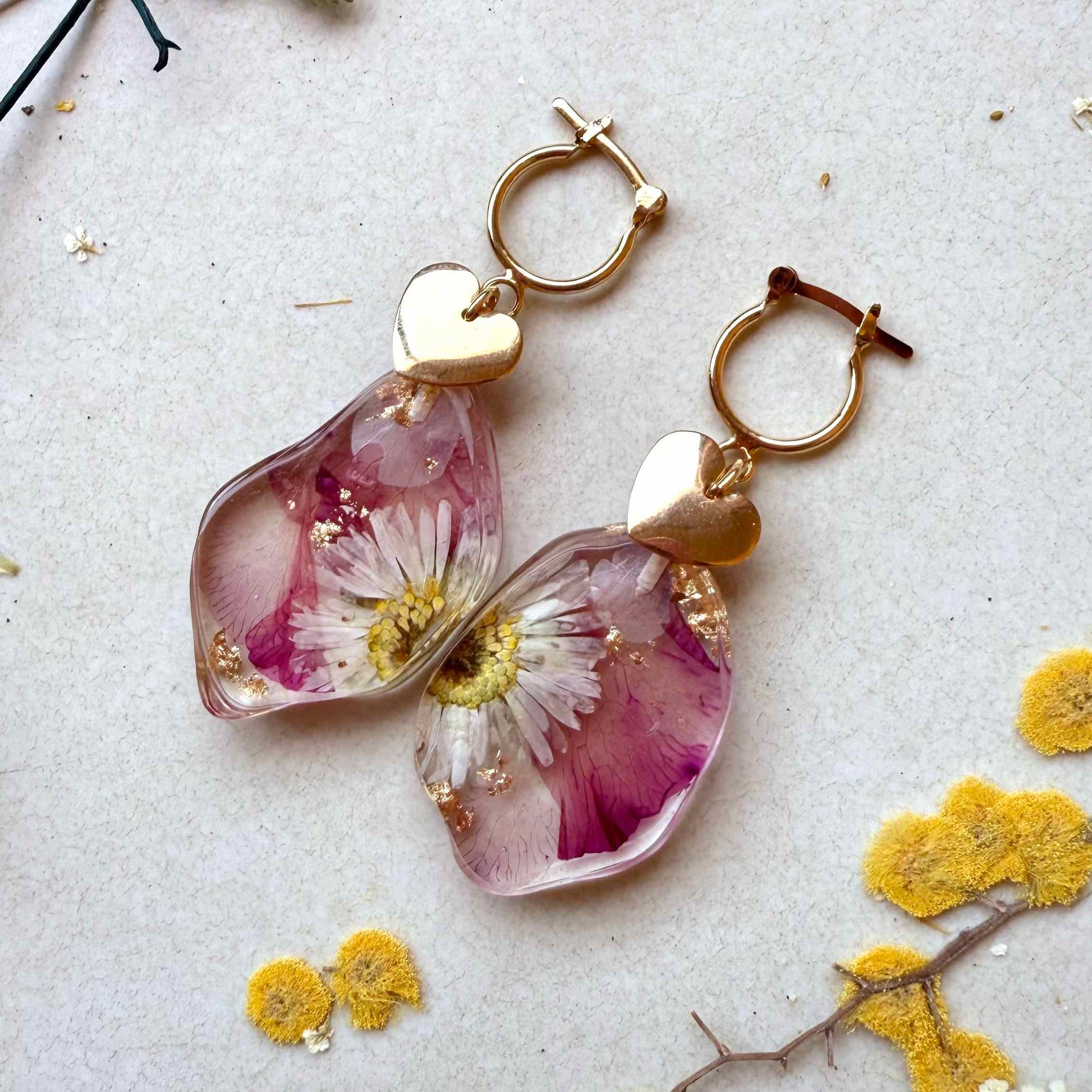 Par de aros Petrohue con fondo blanco. Cápsulas con flor margarita y pétalos de adelfa.